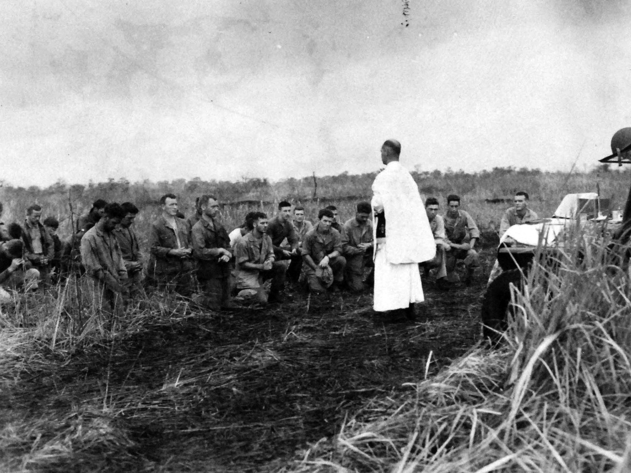 127-GW-983-69000:  Battle of Cape Gloucester, New Britain, December 1943-January 1944.  Marines kneel to worship God in the wilds of New Britain.  They were with the Marines that invaded Cape Gloucester the day after Christmas.  The altar is a jeep and there are bomb craters in the fields behind them, 26 December 1944.  Official U.S. Marine Corps Photograph, now in the collections of the National Archives.   (2014/7/9).