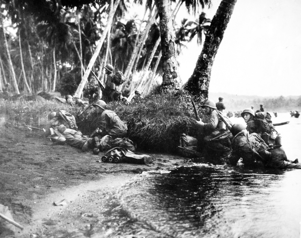 80-G-52573:  Rendova Island Invasion, June 30, 1943.   Attacking a the break of day in a heavy rainstorm, the first Americans ashore huddle behind tree trunks and any other cover they can find.  Official U.S. Navy Photograph, now in the collections of the National Archives.  (2018/04/04).