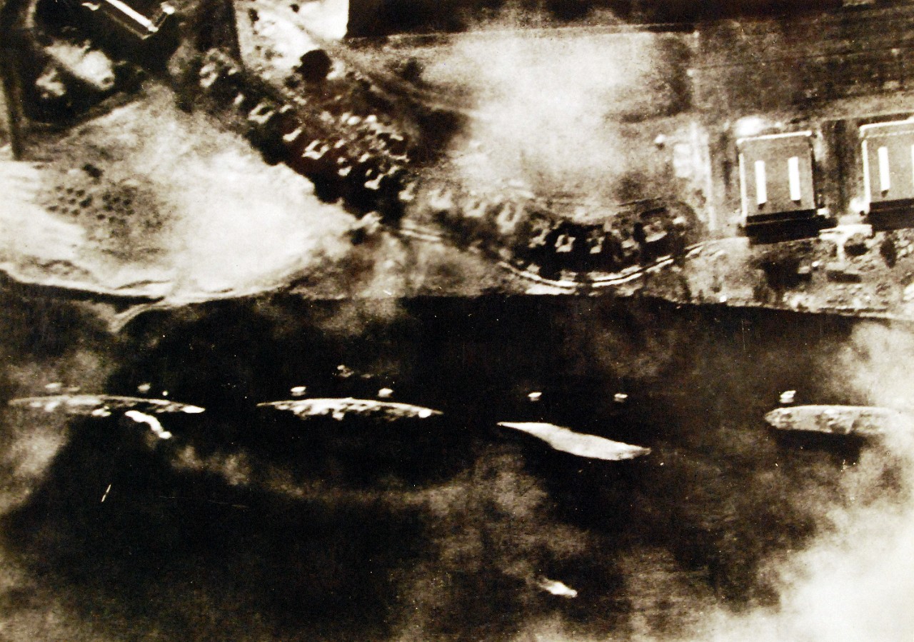 80-G-30553:  Pearl Harbor Raid, December 1941.  Photograph of the western side of Ford Island and ships in moorings offshore, taken from a Japanese Navy plane during the attack. Ships are (from left to right):  USS Detroit (CL-8); USS Raleigh (CL-7), listing to port after being hit by one torpedo; USS Utah (AG-16), capsized after being hit by two torpedoes; and USS Tangier (AV-8), Japanese writing in the lower left states that the photograph's reproduction was authorized by the Navy Ministry.  Also at NHHC as NH 50933.  Translated Japanese caption reads, “The force of enemy ships on the Northwest side of Ford Island destroyed by our violent attack.  The enemy vessels moored on the northwest side of Ford Island opposite the battleships were also violently attacked and put out of action by our assault force.  From the left of the photographs two heavy cruisers are both listing badly.  The white object seen next to them is the bottom of a completely capsized ship.  On the right side of the wreckage of the training ship Utah is a specially-built seaplane tender.  The pair of square objects alongside this vessel are mooring posts.  (9/22/2015).