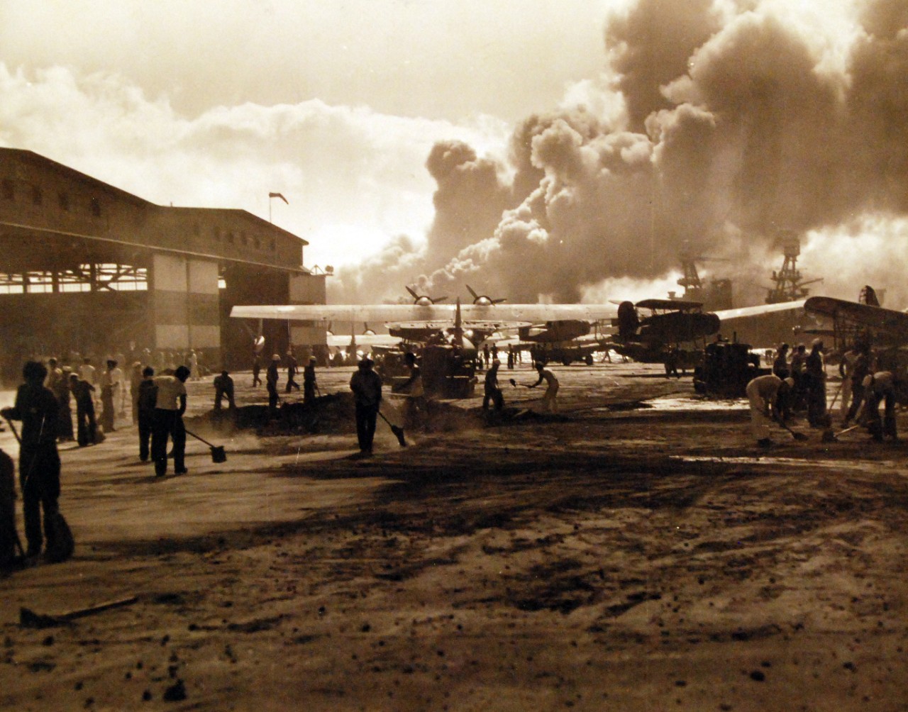<p>80-G-32439: Japanese Attack on Pearl Harbor, December 7, 1941. Sailors stand amid wrecked planes at Ford Island seaplane base, watching ship exploding in the center background.&nbsp;</p>
