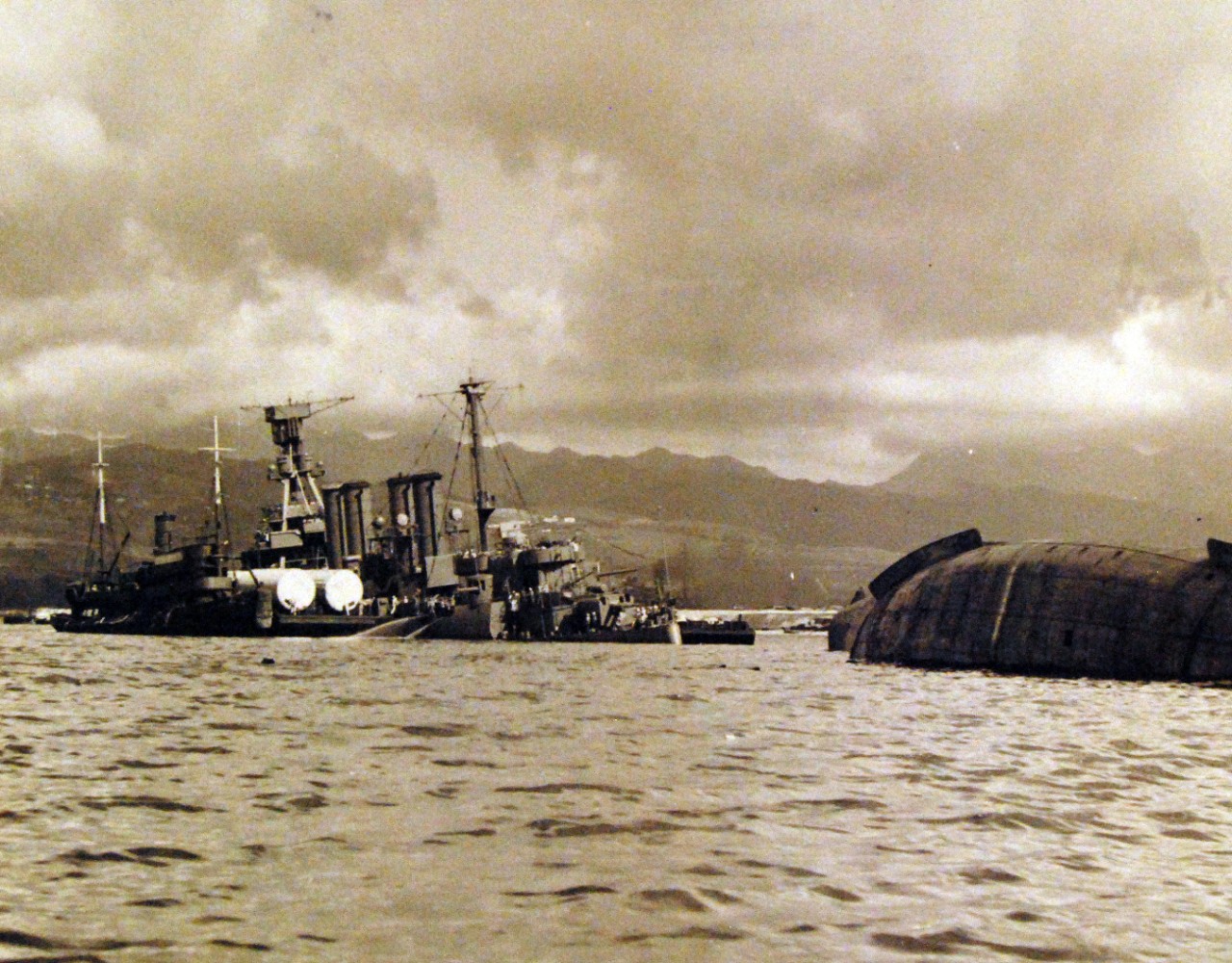 80-G-32742:   Japanese Attack on Pearl Harbor, December 7, 1941.   The capsized USS Utah (AG 16) and USS Raleigh (CL 7) are shown after the attack. Official U.S. Navy photograph, now in the collections of the National Archives. (9/9/2015).
