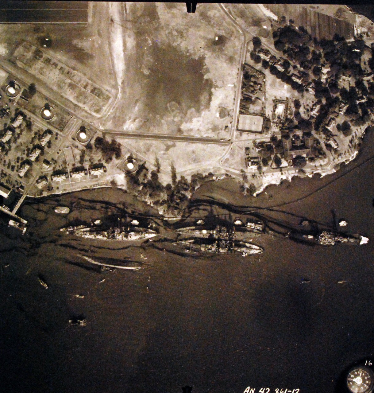 80-G-387573:  Pearl Harbor Attack, 7 December 1941.  Aerial view of "Battleship Row" moorings on the southern side of Ford Island, 10 December 1941, showing damage from the Japanese raid three days earlier.  Diagonally, from left center to lower right are: USS Maryland (BB-46), lightly damaged, with the capsized USS Oklahoma (BB-37) outboard. A barge is alongside Oklahoma, supporting rescue efforts. USS Tennessee (BB-43), lightly damaged, with the sunken USS West Virginia (BB-48) outboard. USS Arizona (BB-39), sunk, with her hull shattered by the explosion of the magazines below the two forward turrets. Note dark oil streaks on the harbor surface, originating from the sunken battleships. Photographed by VJ-1 at an altitude of 3,000 feet and released November 9, 1950.  U.S. Navy photograph, now in the collections of the National Archives.     (9/22/2015).