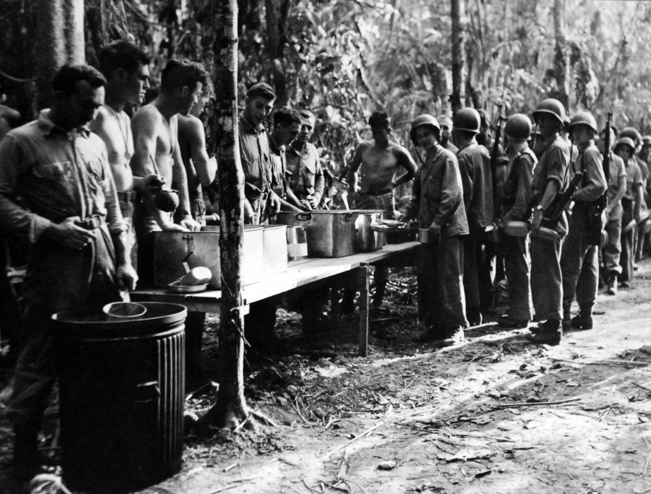 LC-Lot-801-14:  Guadalcanal Campaign, 7 August 1942 – February 9 1943. U.S. Marines line up for a meal which is served cafeteria style.  This picture was taken shortly after U.S. Forces had blasted the Japanese out of several of their positions on the islands.   U.S. Marine Corps Photograph.  Photographed through Mylar sleeve.  Courtesy of the Library of Congress.  (2015/11/06).