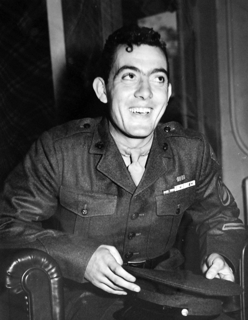 LC-Lot-801-35:  Guadalcanal Campaign, August 1942 – February 1943. Press Query About Hero’s Father Brings a Smile.   Platoon Sergeant John Basilone, USMC, broke out in this big smile in the pres room at the Navy Department, September 2, 1943, when in the course of an interview, a reporter asked about his Italian-born father.  Asked what his father thought of him serving in the Marines, Basilone smiled and answered simply, “My father likes this country.”  The Marine sergeant was awarded the Medal of Honor for his actions at Guadalcanal.   Basilone later died at the Battle for Iwo Jima, February 19, 1945, during that D-Day invasion.  U.S. Navy Photograph.    Photographed through Mylar sleeve. Courtesy of the Library of Congress.  (2015/11/06).
