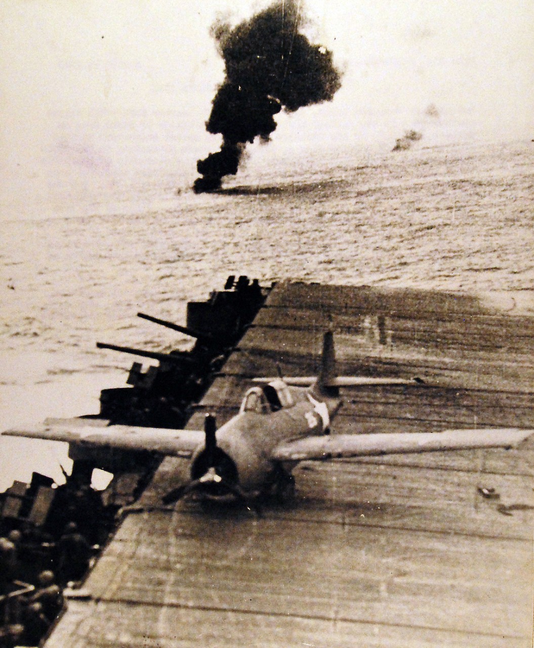 80-G-42560:   Battle of Santa Cruz Islands,  26 October 1942.    Scene from the flight deck of USS Enterprise (CV 6).  Shaken loose from its moorings by the powerful explosion of a Japanese bomb which hit in the water near Enterprise, this U.S. plane skitters to the edge of the carrier’s flight deck.  Note, the column of smoke sent up by a downed Japanese plane in the background.   Photographed October 26, 1942.  Official U.S. Navy photograph, now in the collections of the National Archives.  (2016/05/17).