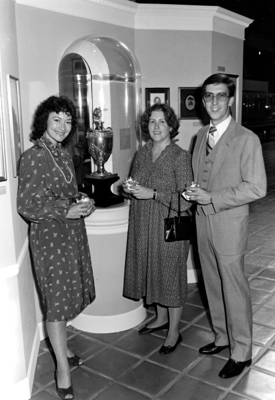 NMUSN-Photo-4:   Mrs. Claudia Pennington (left), Navy Memorial Museum (now National Museum of the Navy) staff member with husband, (right), and unidentified female invitee (center).     They were attending the opening of the exhibit, A Special Relationship: United States Navy and United Kingdom Royal Navy,  held at the museum, October 1984.  National Museum of the U.S. Navy Photograph Collection.  
