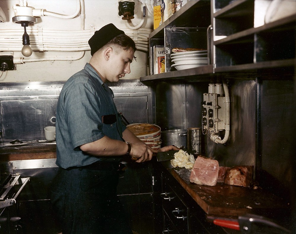 Submarine Galley Scene. Cook cutting lettuce, probably for ham sandwiches, in the galley of a U.S. Navy submarine, during World War II. Photographed by Edward Steichen. Official U.S. Navy Photograph, now in the collections of the National Archive...