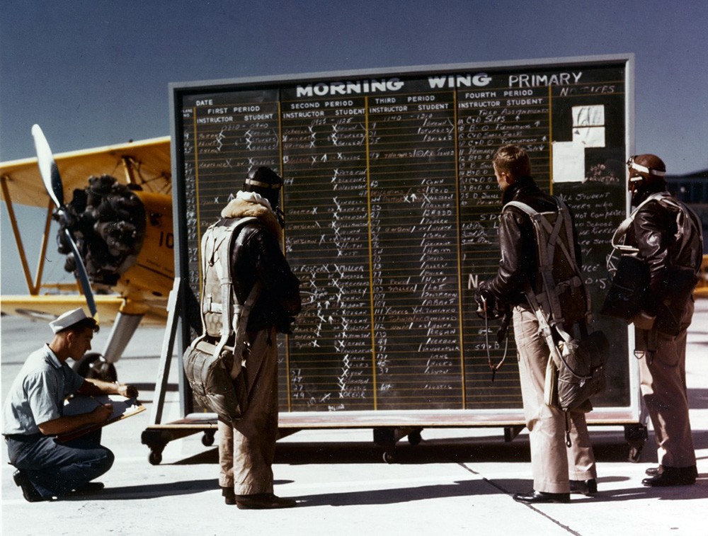 Naval Aviation Cadet Training, circa 1942-43.   Flight instructors and naval aviation cadets check the operations board for the morning flight schedule, at a naval air station.  Note the Stearman N2S parked behind the board.   Official U.S. Navy Photograph, now in the collections of the National Archives, 80-G-K-15048