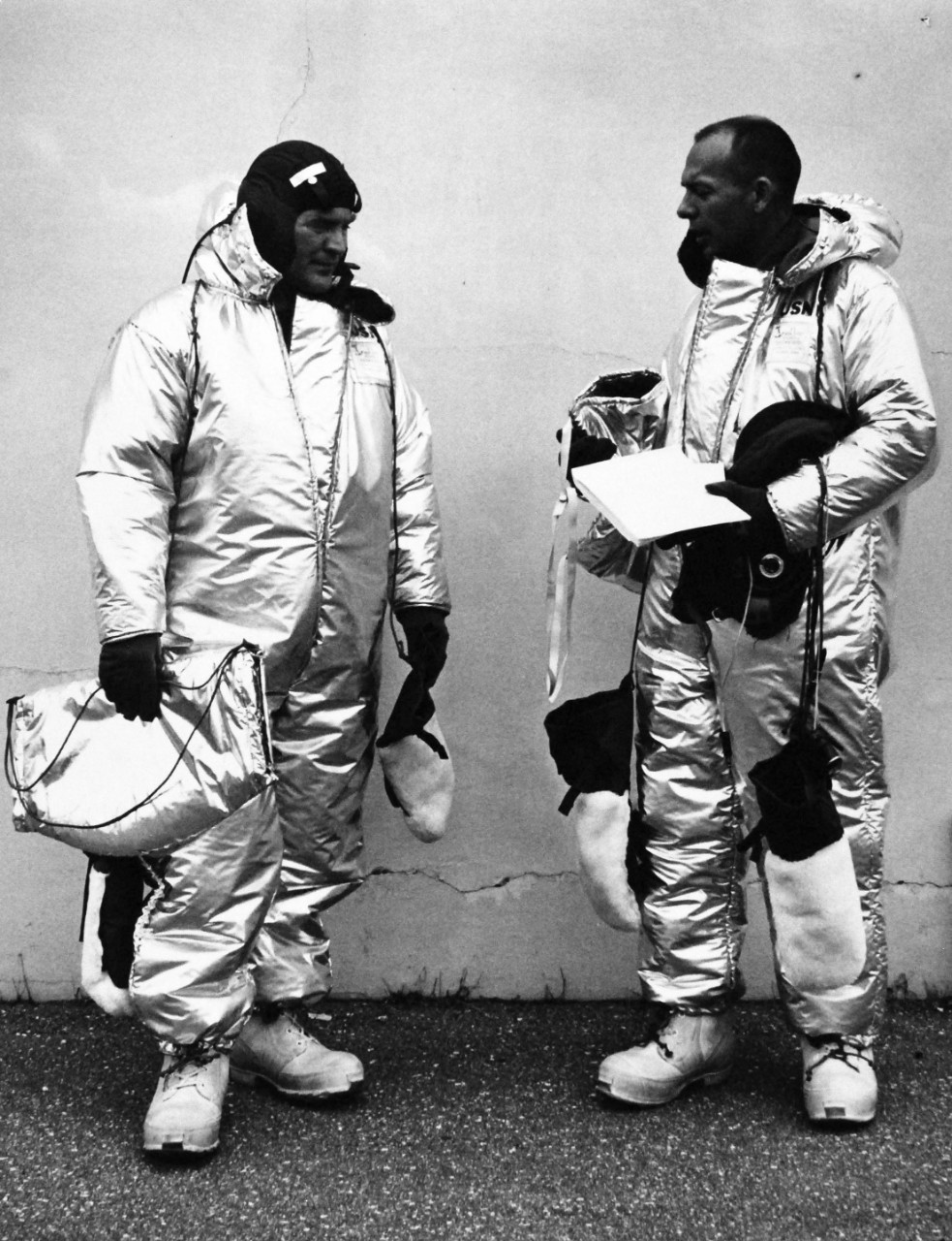 Navy Balloonists To Test New Cold Winter Space Suits.   Commander M.D. Ross, USNR, right, U.S. Navy Balloon Pilot, discusses his newly designed cold weather space suit with Mr. Cooper, Flight Scientist of the High Altitude Observatory, University of Colorado.  The two astronomers will use the new suits on their balloon and on a gondola by atmosphere flight from the Stratobowl Laboratory near Rapid City, South Dakota, planned for 1 August 1959.  The Strato Lab flight is one of the continuing series planned by the Office of Naval Research.  Primary insulating assembly on the new garment consists of two rubberized fabrics coated with a thin aluminum film a string-like plastic spacer holds the two fabrics apart.  This arrangement provides good insulation and reduces heat transferred radiation.  The cold weather uniform was developed by the clothing division of the U.S. Navy Supply Research and Development Facility.   Official U.S. Navy photograph, now in the collections of the National Archives.     