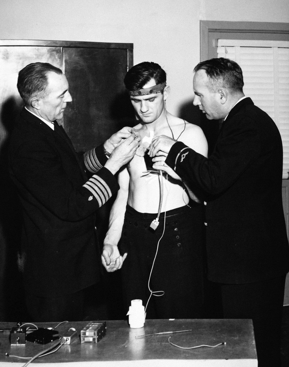 330-PS-8850-2:  U.S. Navy Conducts Physical Studies By Telephone.  Captain Norman Les Barr, MC, USN, Hospitalman Ralph Form, USN, attaching electrodes Electrician’s Mate First Class A.L. Monroe, USN, March 21, 1958.  Official Department of Defense photograph, now in the collection of the National Archives.   