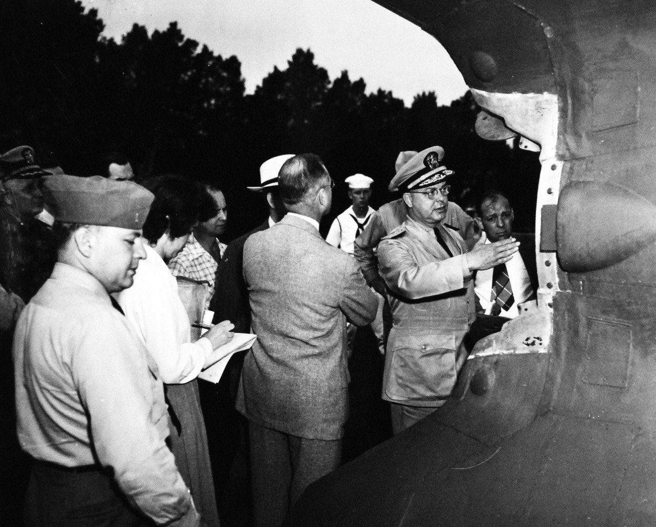 80-G-49885:   German V-2 Rocket being shown by the U.S. Navy in Washington, D.C.   This bomb measured 45’ in length and was captured intact near Nordhausen, Germany.  Rear Admiral Willard A. Kitts explains the details of the tail mechanism which controls the bomb while in flight.   Photograph released July 10, 1945.  Official U.S. Navy Photograph, now in the collections of the National Archives.    
