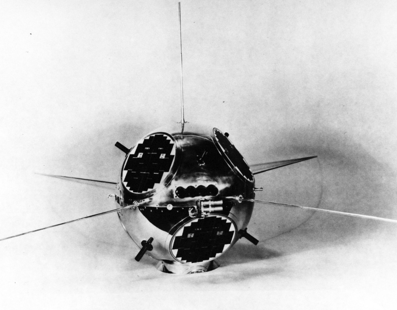 USN 711007:  The Naval Research Laboratory’s Solar Radiation IV will monitor x-ray radiation from the Sun and ultraviolet radiation in the night sky.  Visible in the photograph are:  three solar cell patches; one of the sphere’s four x-ray detectors (dark vertical line on left side of ball’s equator); the four parallel gun-barrel-like ultraviolet detectors; the six Earth-aspect detectors (dark tube-like attachments or horns jutting out diagonally from the sphere); the two small gas satellite’s equator; half of the four miniature rocket backup spin-up satellites making up the payload of Composite I.  Photograph released January 24, 1962.  Official U.S. Navy Photograph, now in the collections of the National Archives.  