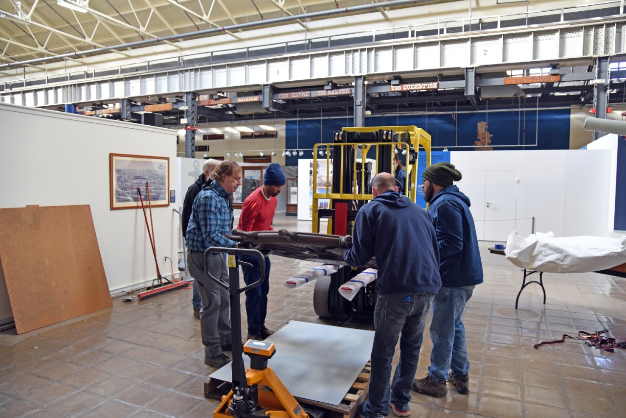 NMUSN-5141: Protected cruiser Albany’s Helm Wheel, December 2022. Museum staff discusses how to remove the wheel from the forklift to a resting position. Shown, left to right: Museum Specialist Tom Potthast, Museum Curator Eddie Valentin, Collect...