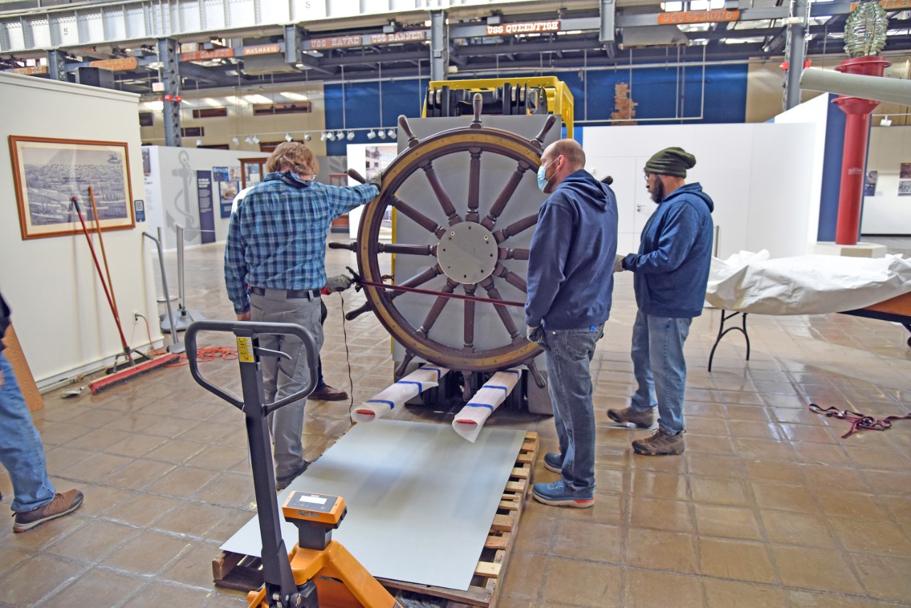 NMUSN-5140: Protected cruiser Albany’s Helm Wheel, December 2022. Museum staff discusses how to remove the wheel from the forklift to a resting position. Shown, left to right: Museum Specialist Tom Potthast, Collections Manager Wesley Schwenk, an...