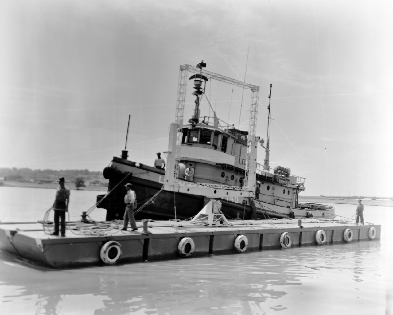 NMUSN-1019:   XAF Radar Antenna, 1960s.   Being delivered to the Washington Navy Yard for display.  Note the U.S. Navy tug alongside a small thin barge carrying the radar antenna.  The tug appears to be USS Wahtah (YTB-140).  This radar was the first shipboard radar to be installed onboard a U.S. Navy ship, USS New York (BB-34).  Surviving World War II, it was brought to the Washington Navy Yard where it was on exterior display until the mid-1980s where it was placed into storage.   Following conservation, the radar is now on display at the National Electronics Museum, Linthicum, Maryland.    Original is a black and white negative.   National Museum of the U.S. Navy Photograph Collection.