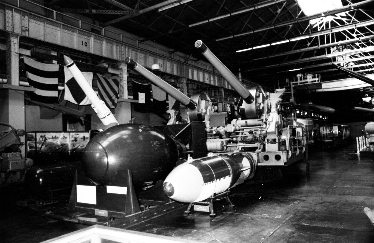 NMUSN-791: Weapons Display area, mid-1970s. Area shows the various weapons on display in Bay 10 area, including Fat Man, the 5” gun and from USS Reno (CL-96) (without cover). National Museum of the U.S. Navy Photograph Collection.