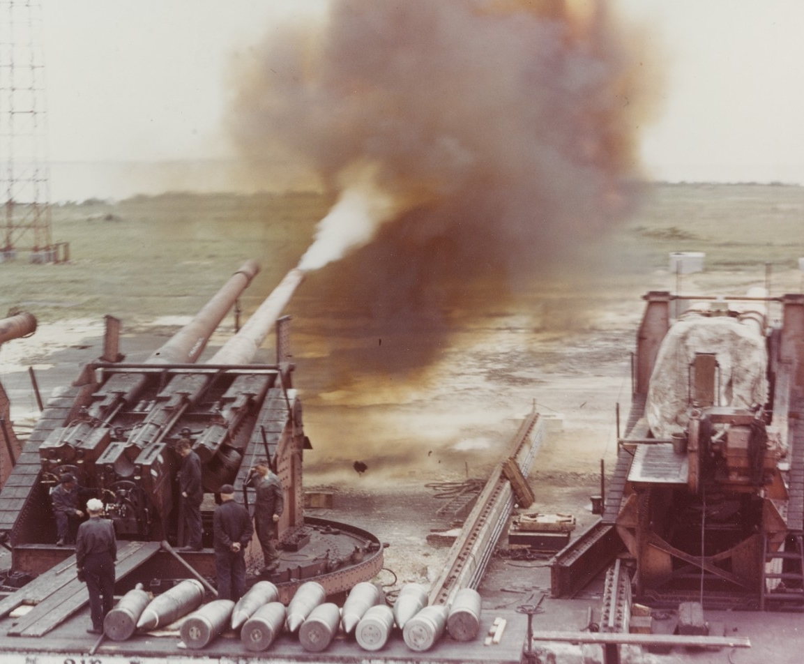 Image:  Firing of an eight-inch, 55-cal. Gun, during tests in World War II. This is a triple, single sleeve gun mount, with the right barrel removed. Shells on stand in foreground are of about 16" size, possibly for the 16" gun at right.  Courtesy of the National Archives