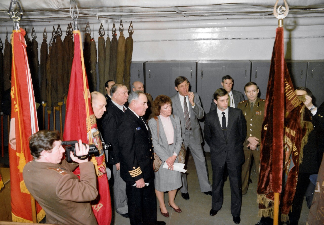 NMUSN-130:   American Military Museum Directors, Moscow, Russia, February-March 1989.   Directors tour a Soviet Military Museum.   The Navy Museum’s Director Oscar P. Fitzgerald, Ph.D., is second from left, back row.   Deputy Director Ms. Claudia Pennington is fifth from left.   Naval Aviation Museum Director Robert L. Rasmussen, is fourth from left.   This photograph was taken following the Soviet Military Museum contingent which visited the United States in December 1988.   The Chairman of the U.S. Joint Chiefs of Staff and his Soviet counterpart, Marshal of the USSR, Sergei F. Akrohomeyev, approved an exchange of military museum directors in 1987.  This exchange promoted better understanding between the two countries.    National Museum of the U.S. Navy Photograph Collection.  
