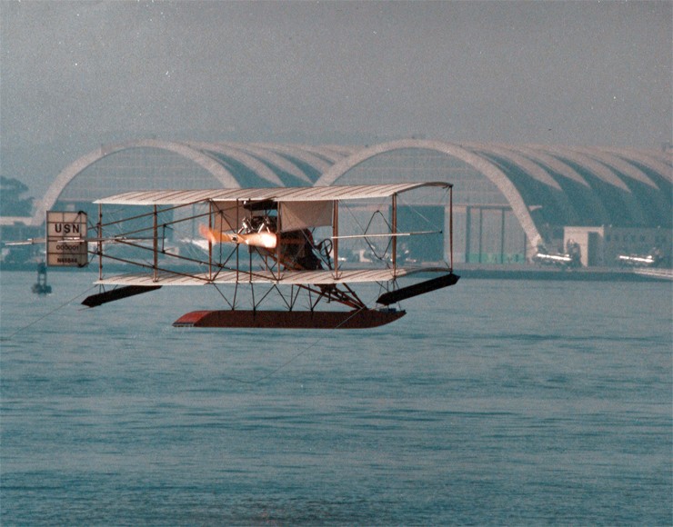 Photo of replica of the Navy's first aircraft flying over San Diego Bay.