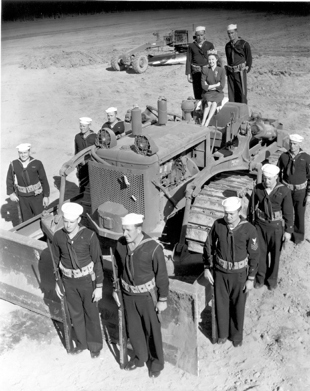 <p>Susan Hayward perched on top of her throne – a symbolic Seabee bulldozer - is crowned the first Seabee Queen by the enlisted men of CBMU 515, November 1943. The first “Queen of the Seabees” was officially welcomed to Camp Rousseau by Capt. H.P. Needham, CEC, USN, and crowned by F1c Clarence Wofford and MM2c William Murray.</p>

