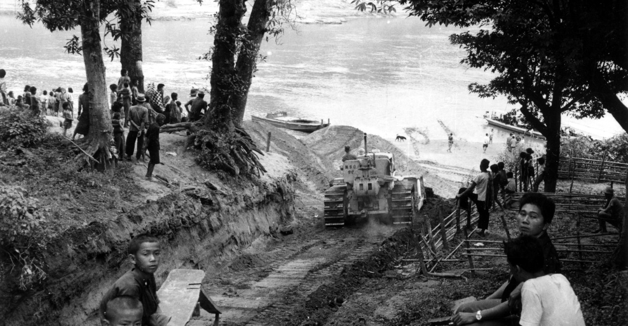 Seabee Technical Assistance Team 1103 constructs a road in Nam Pat out of an ox trail, 1964.  STAT team operations in Thailand began in 1963 at the request of the Royal Thai Government. The Seabees were employed in support of Thailand’s Accelerated Rural Development program to teach Thai nationals the trades of construction, equipment operations, maintenance, road surveying, and heavy bridge and dam construction. 