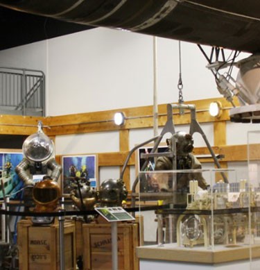 interior view of some of the exhibits at the Naval Undersea Museum showing some diving suits and a torpedo overhead.