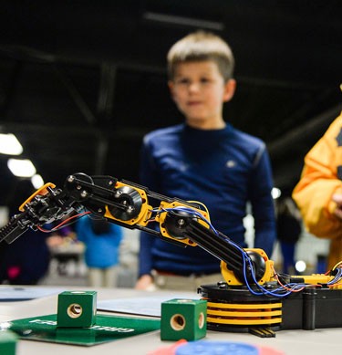 Navy STEM Day: A child looking at a robotic arm durring the learning program