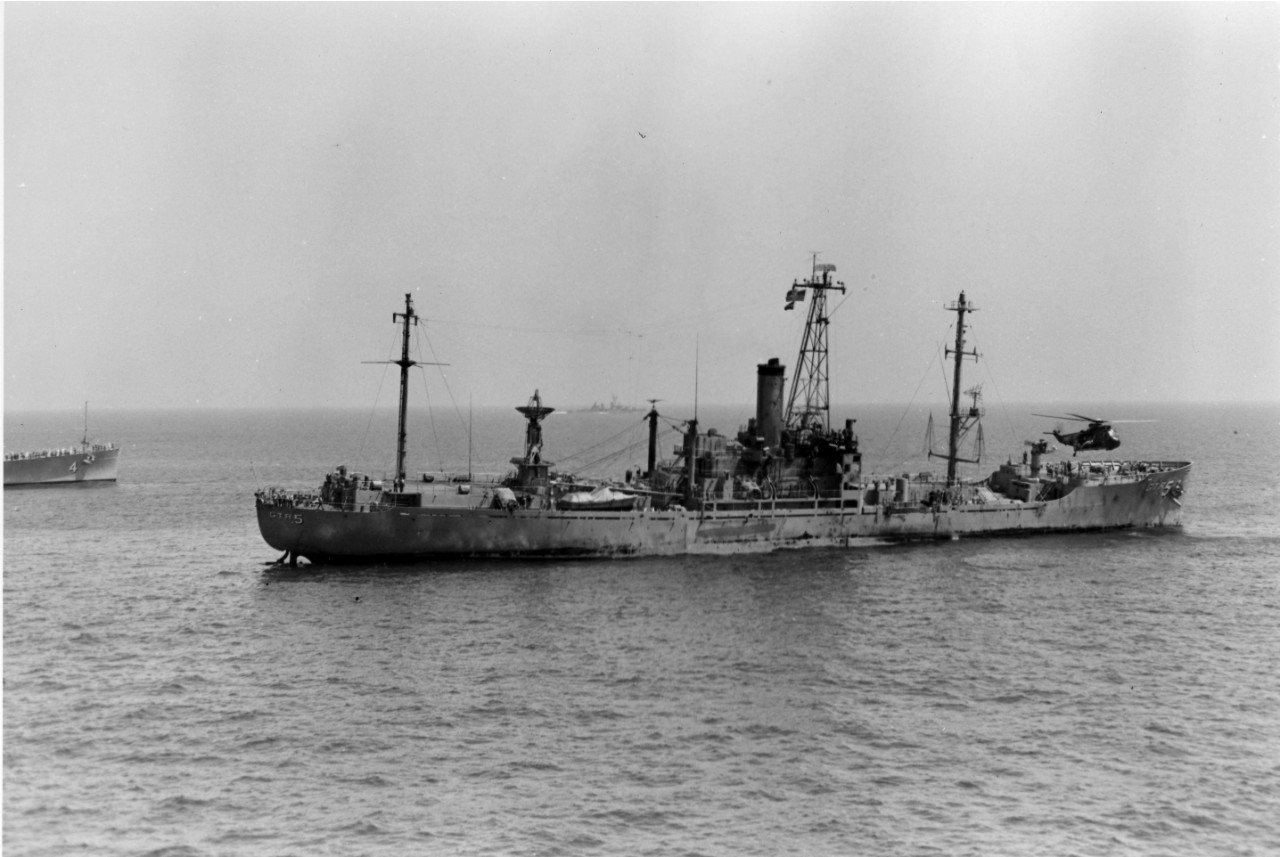 With a decided starboard list, the USS Liberty (AGTR-5), accompanied by the guided missile cruiser USS Little Rock (CLG-4), limps slowly toward the Port of Valletta, Malta, for repairs following the attack by Israeli torpedo and aircraft. The helicopter hovering over the bow of the ship is removing the wounded and dead to the attack carrier USS America (CVA-66). 