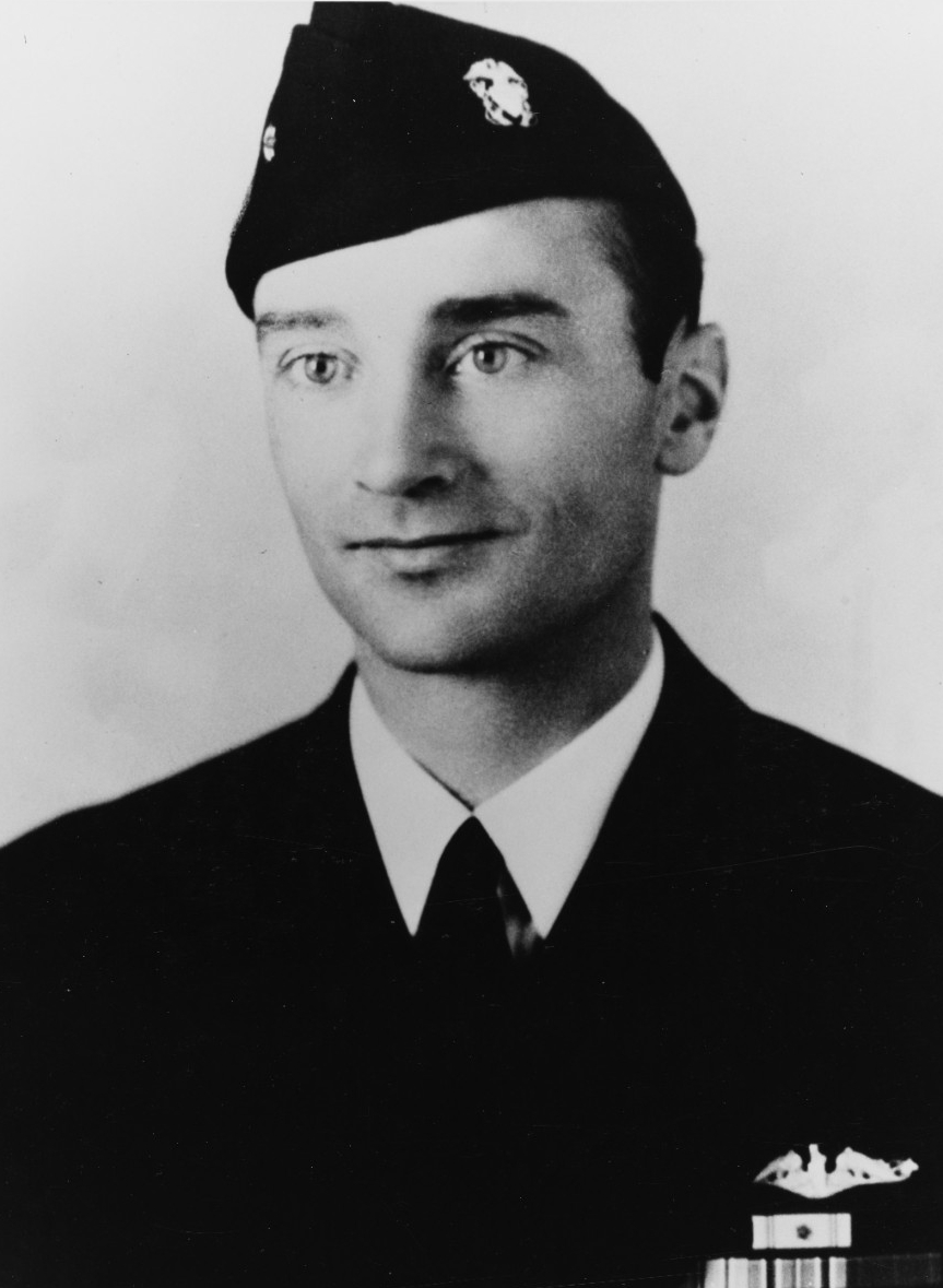 A photographic portrait of Commander Lawrence Lott Edge. Edge faces the camera but looks off to his right, slightly. He is wearing a black officer’s uniform and a black officer’s cap. 