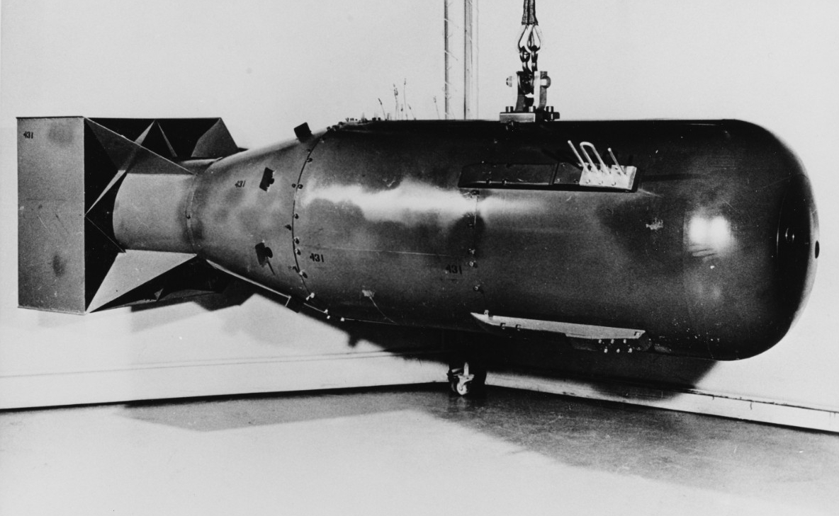 Black-and-white photograph of the “Little Boy” type atomic bomb, the kind detonated over Hiroshima, Japan, on 6 August 1945. The bomb is 28 inches in diameter and 120 inches long. Here, the bomb is photographed indoors. It appears to be suspended from a cable or chain.
