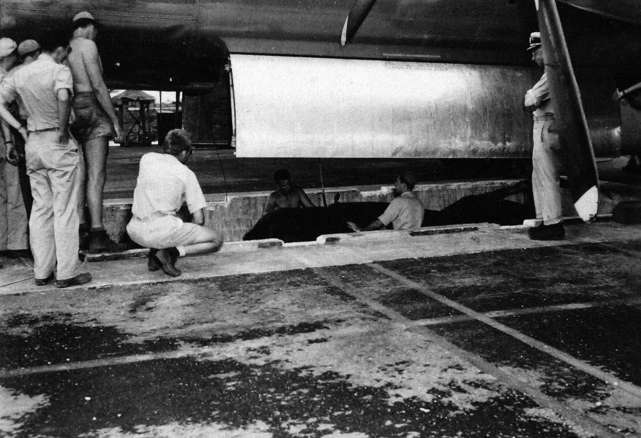 77-BT-130: Tinian Island, August 1945. Side shot of unit in pit, being lined up to hoist Little Boy into bomb bay; canvas cover is still on unit. Lieutenant Wright in pit and Commander A.F. Birch on edge of pit, directing operations. Official pho...