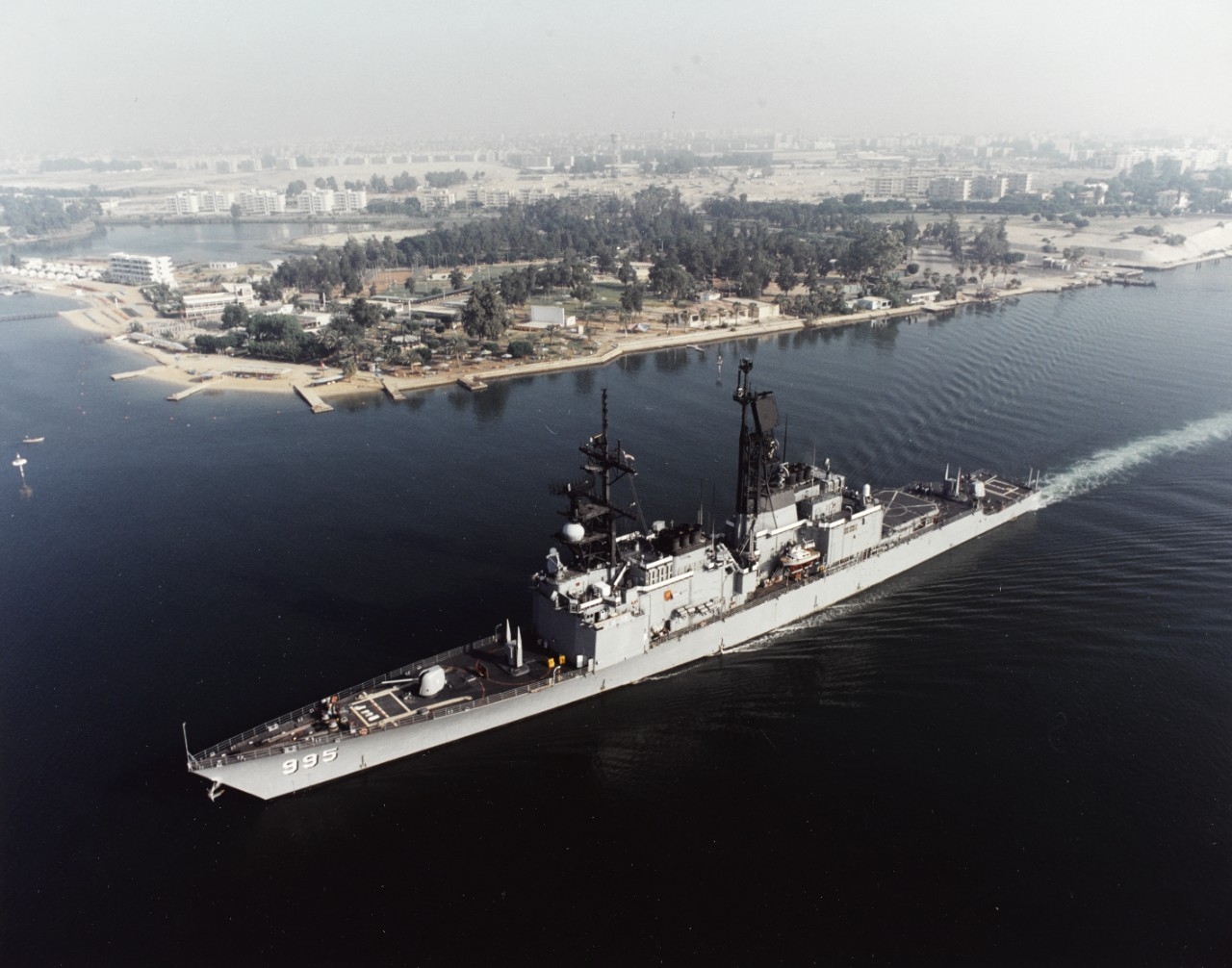 Color, aerial photograph of USS Scott (DG-995) in the Suez Canal. The background shows a sandy shoreline with buildings and trees farther inland. 