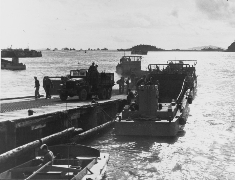 U.S. Navy Seabees unload supplies from trucks and load them aboard LCMs at a pontoon pier near Inchon's tidal basin, 13 October 1950.