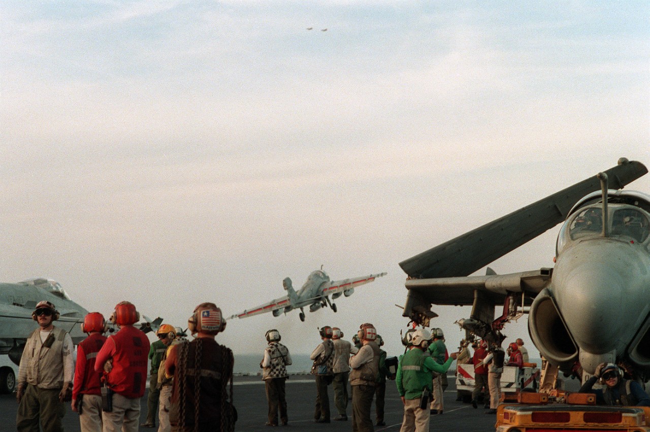 Photo of aircraft carrier with crewmen watching incoming aircraft
