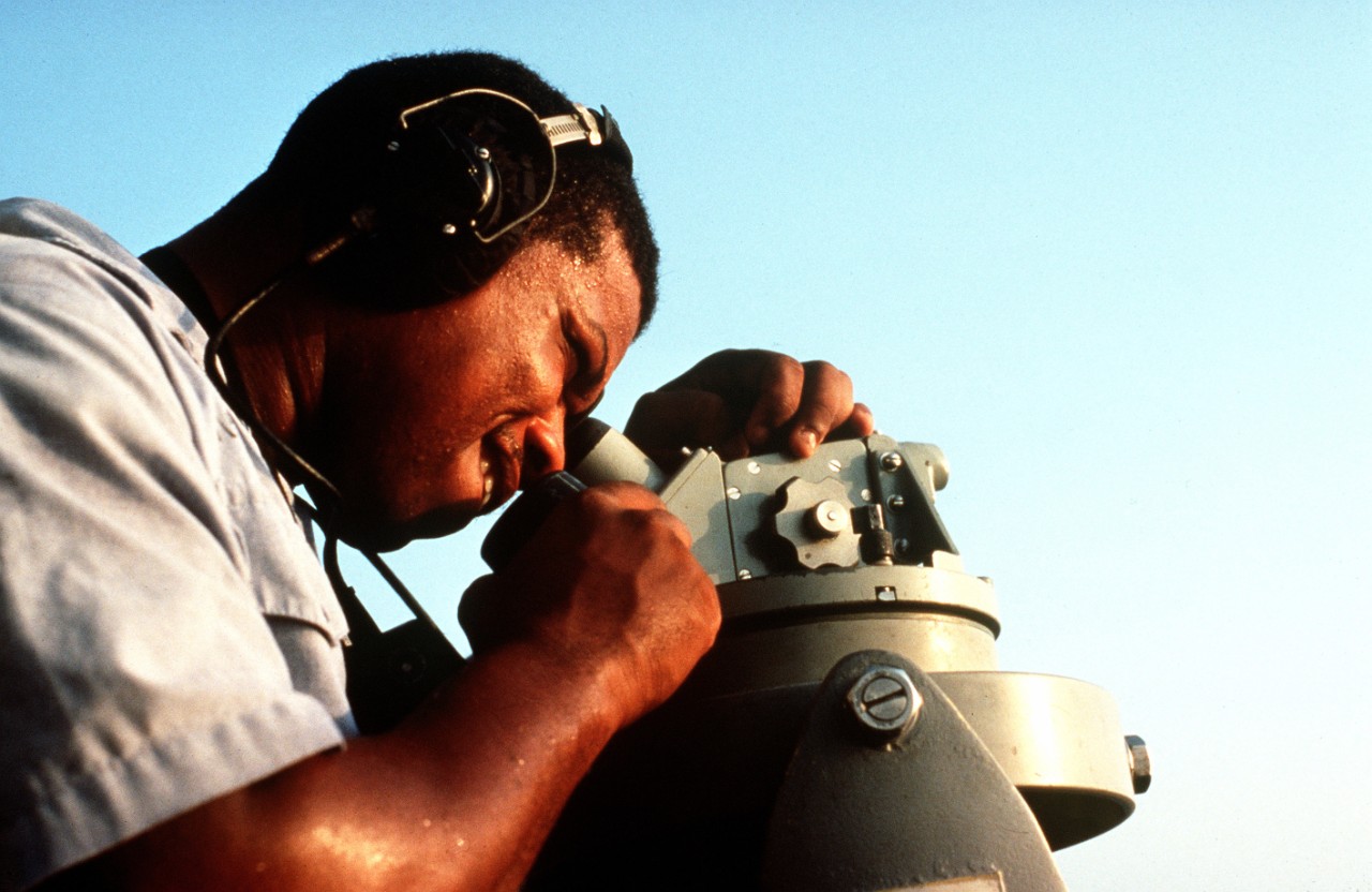 A crewman aboard a minesweeper takes a bearing with a telescopic alidade. 