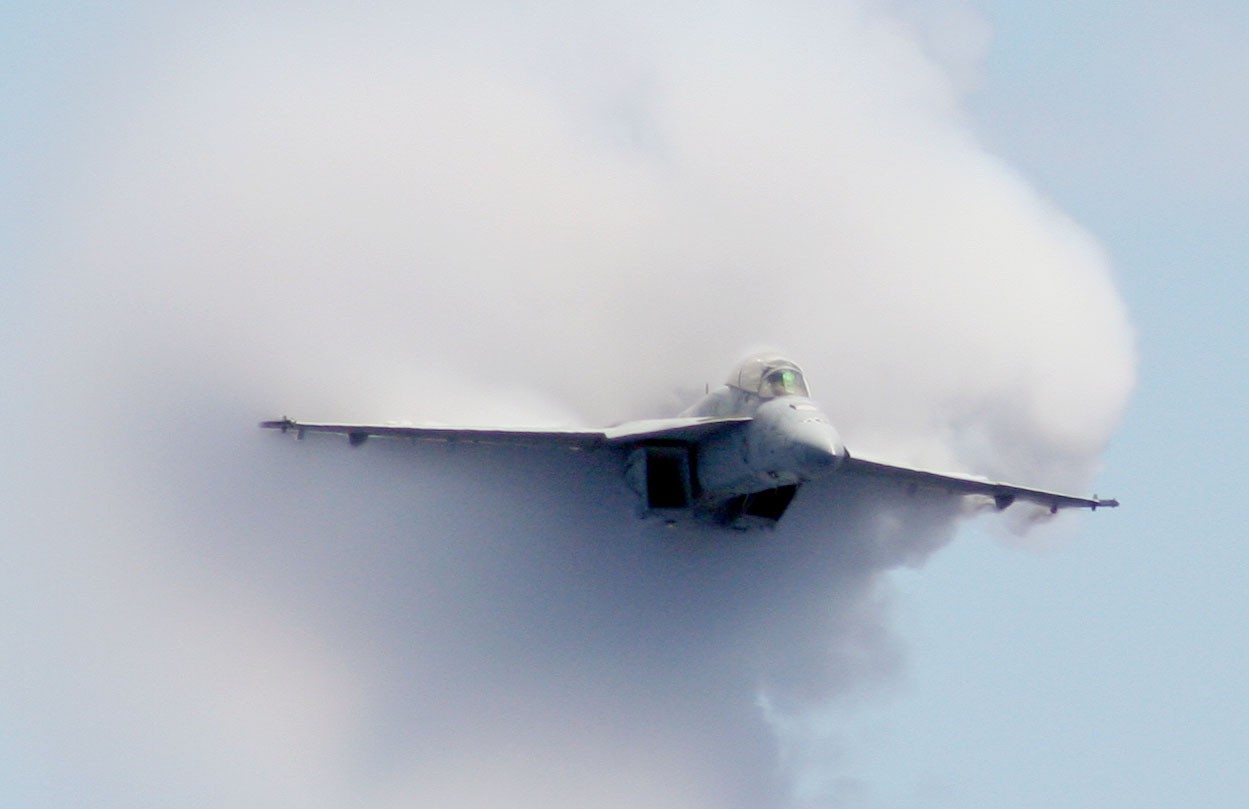 Image of a F/A-18F Super Hornet strike fighter emerging from a cloud. 