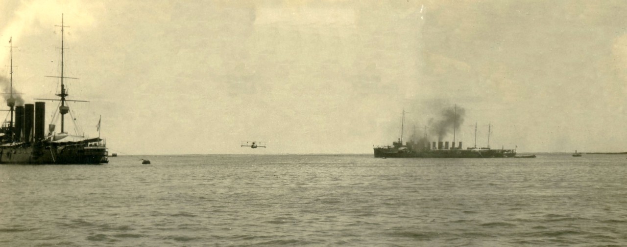 A plane flying low over the water between two vessels afloat. 