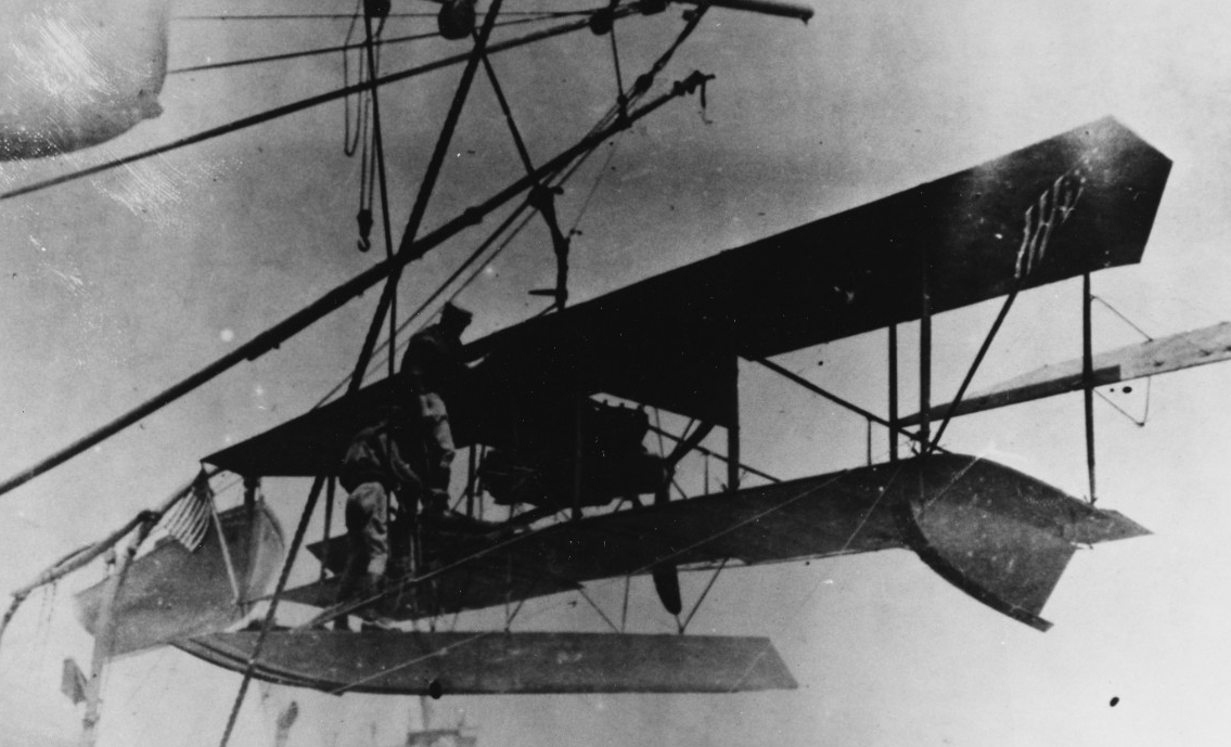 A shipboard extension boom is used to hoist a biplane into the air.