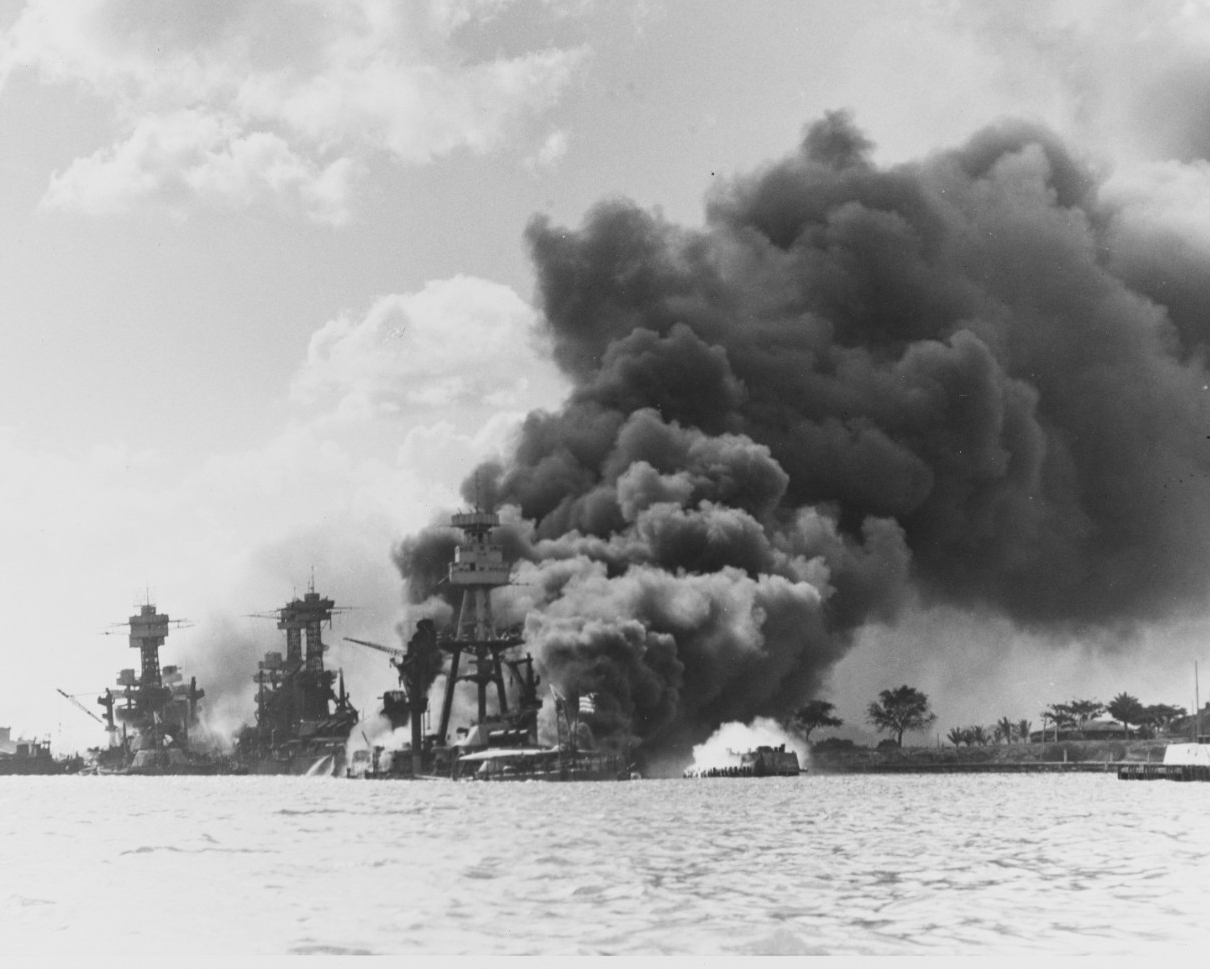 View looking up Battleship Row on 7 December 1941, after the Japanese attack. The sunken and burning USS Arizona (BB-39) is in the center. To the left of her are USS Tennessee (BB-43) and the sunken USS West Virginia (BB-48).