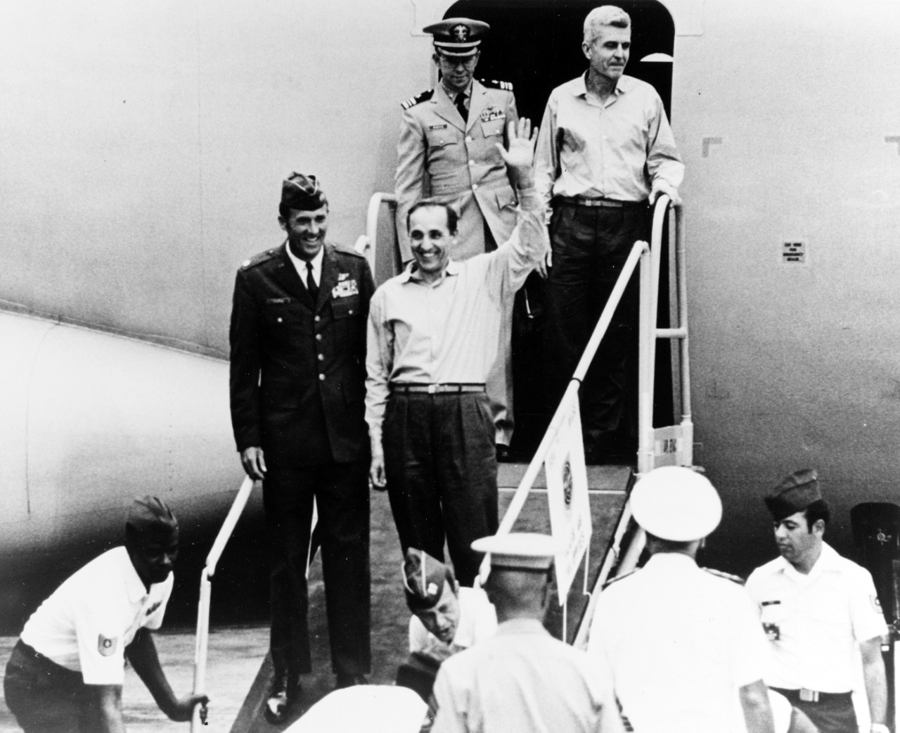 Two of the returned prisoners of war step from the second U.S. Air Force C-141 to leave Hanoi, at Clark Air Force Base, Philippine Islands, in February 1973. They are: Colonel Robinson Risner, USAF (waving), and Captain James Stockdale, USN. Their escorts are Major Leroy W. Thornal, USAF, and Lieutenant Commander Elman J. Parrie, USN.