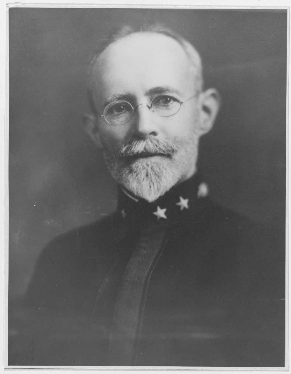 faded black and white portrait of bearded man looking at the camera wearing a uniform and glasses