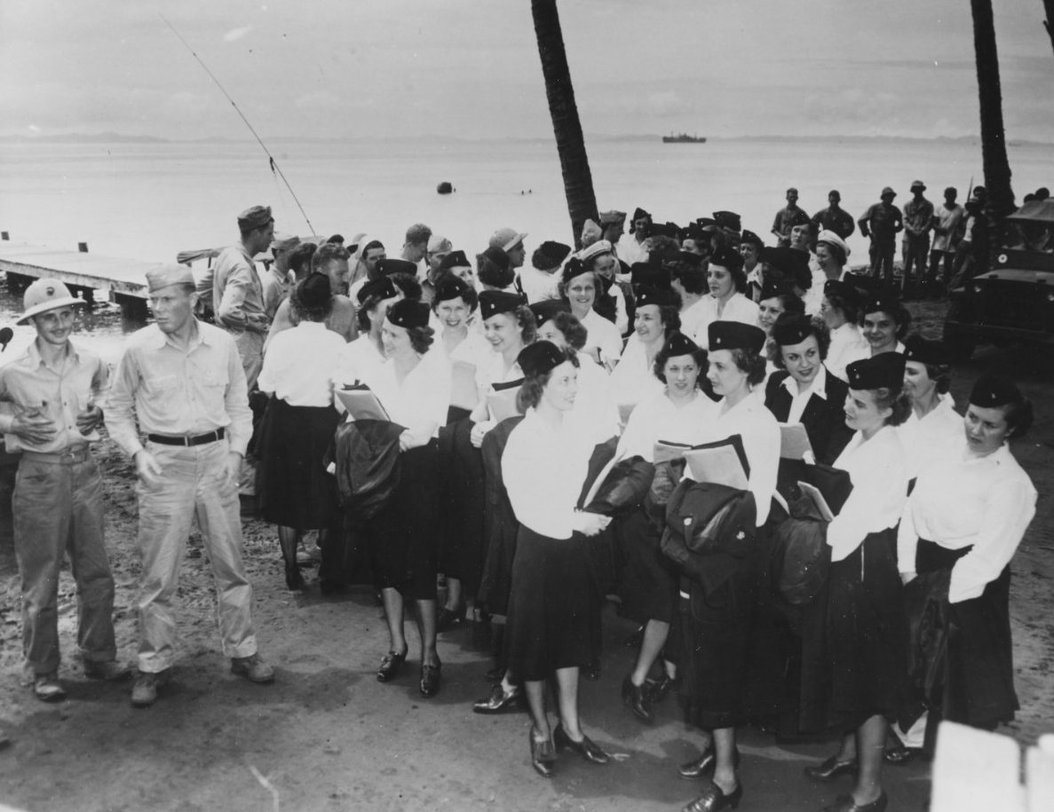 Fifty Navy Nurses in uniform stand on shore next to Marines