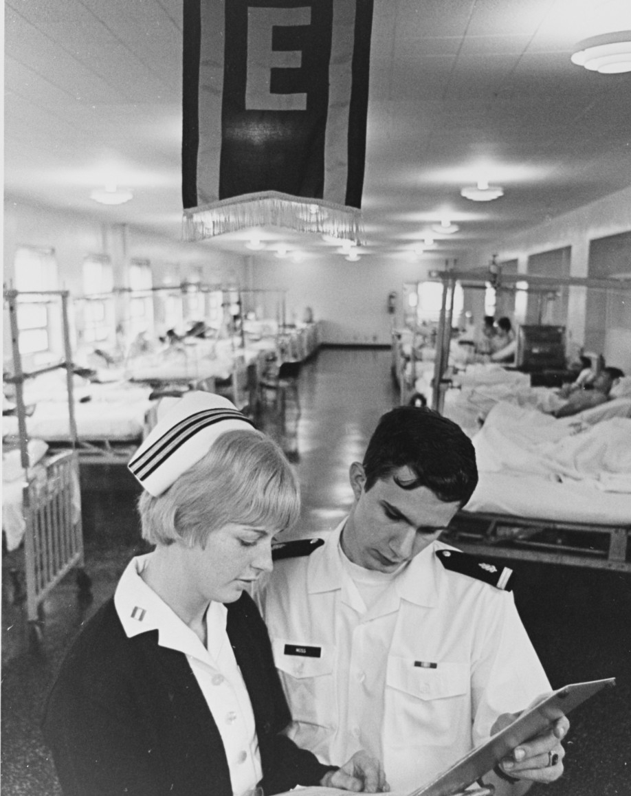 A male nurse in white uniform and a female nurse in uniform review paperwork together.