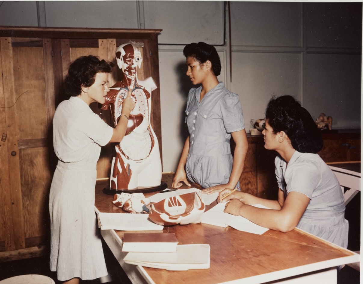 A nurse points to a part of a human anatomy model as two student nurses look on.