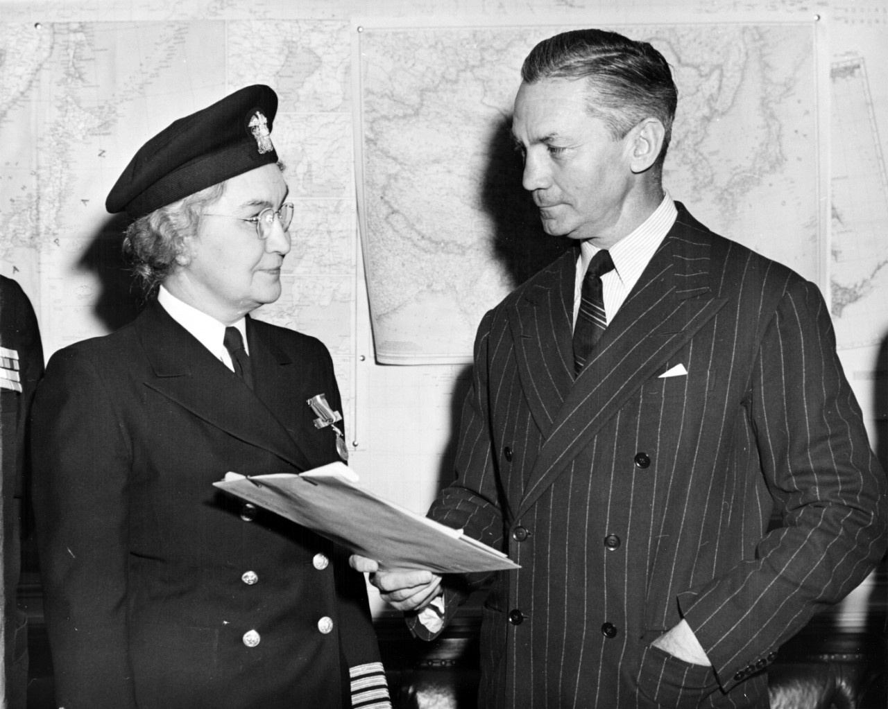 Captain Dauser stands in her blues uniform (with cap) next to a man in a suit holding an award