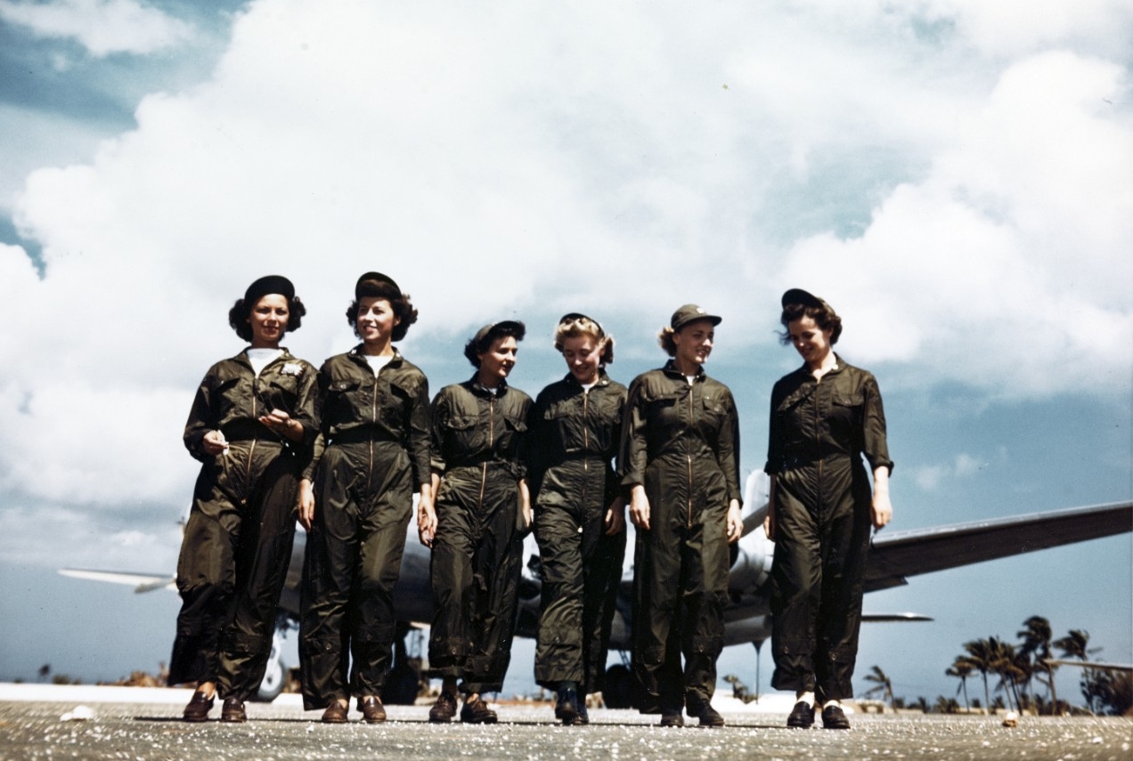 Five women in olive green flight suits walk away from a plane