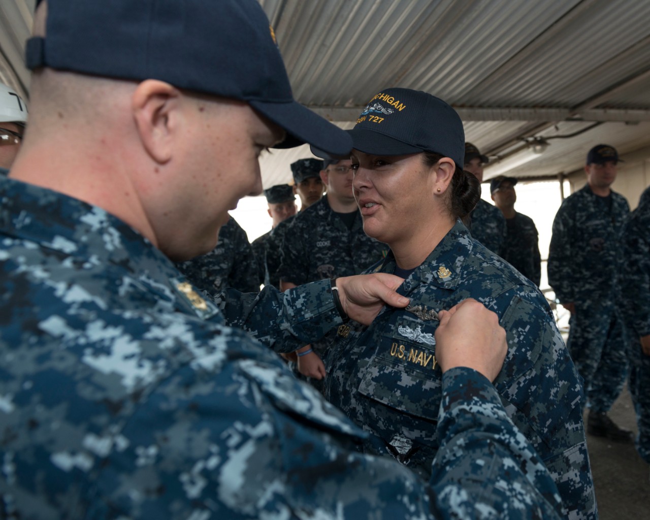 A male sailor pins the submarine warfare pin on a female sailor's uniform.