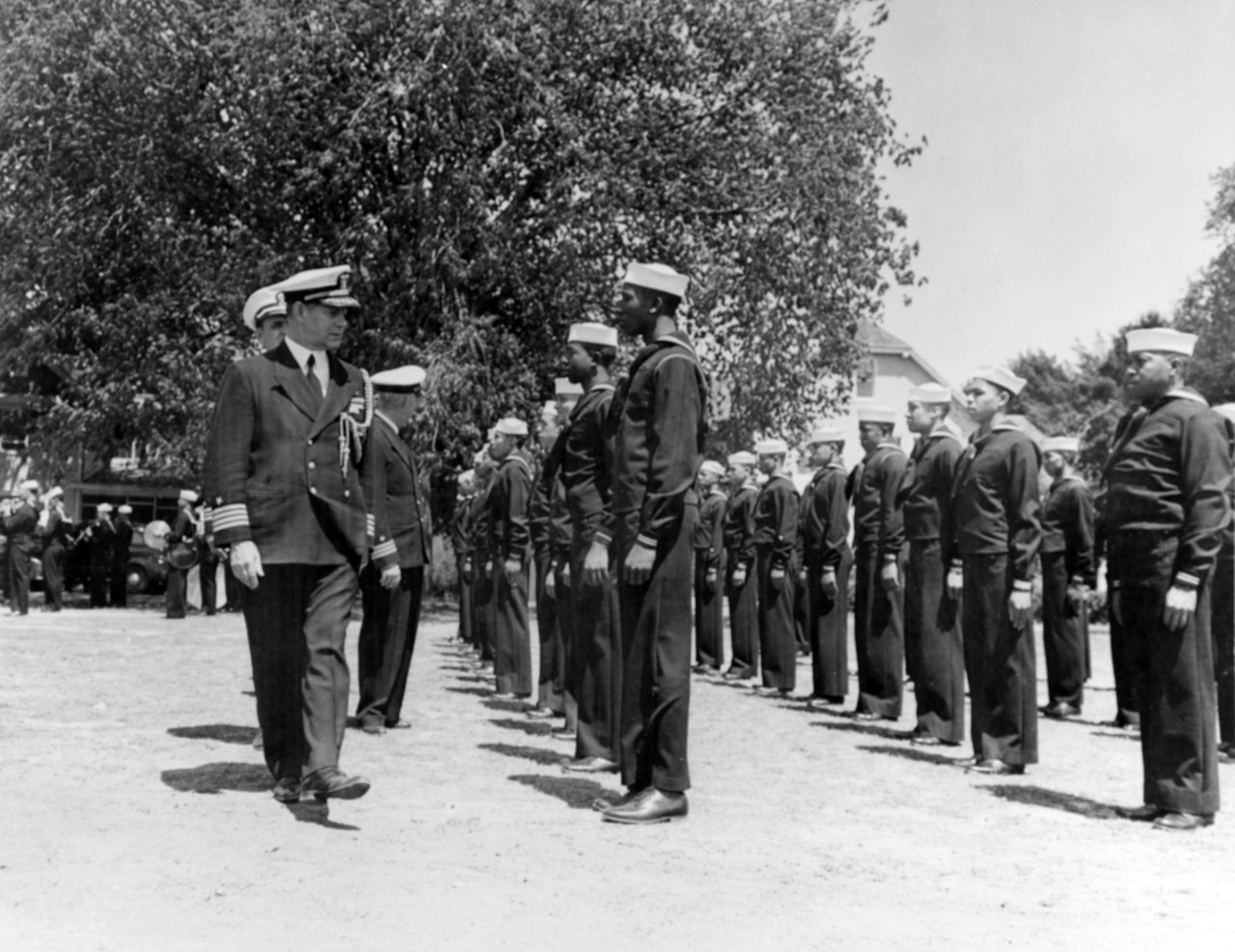 Black men dressed in Navy enlisted uniform arranged in formation with a group of White officers walking along the front line.