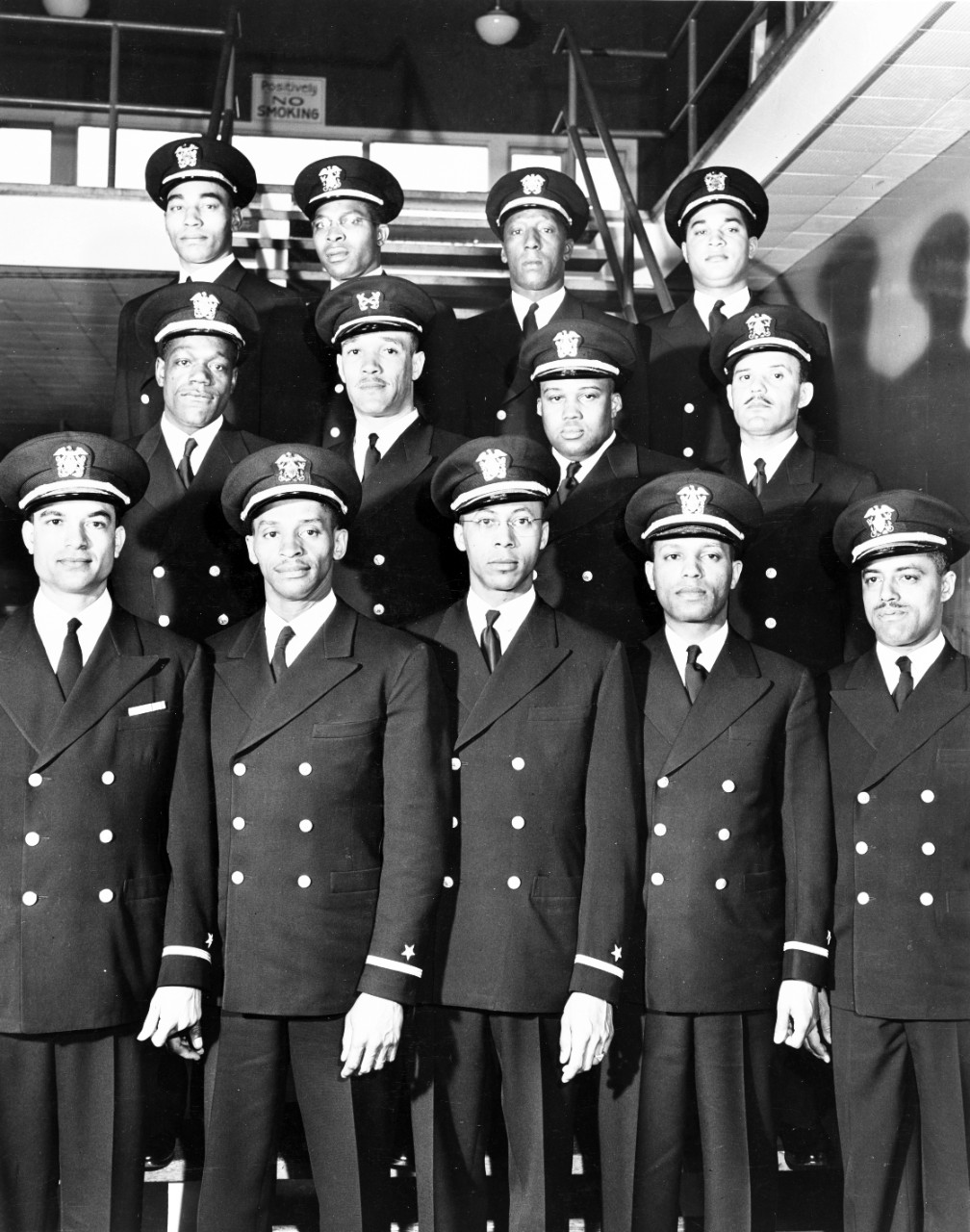 Formal portrait of thirteen African American men in Navy uniform standing in rows on stairs.