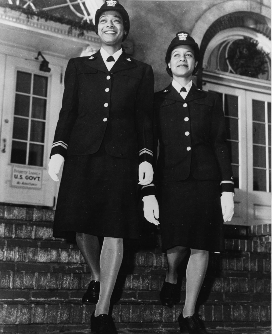 Photograph of two African American women in uniform of the WAVES walking down stairs in front of exterior of a building.